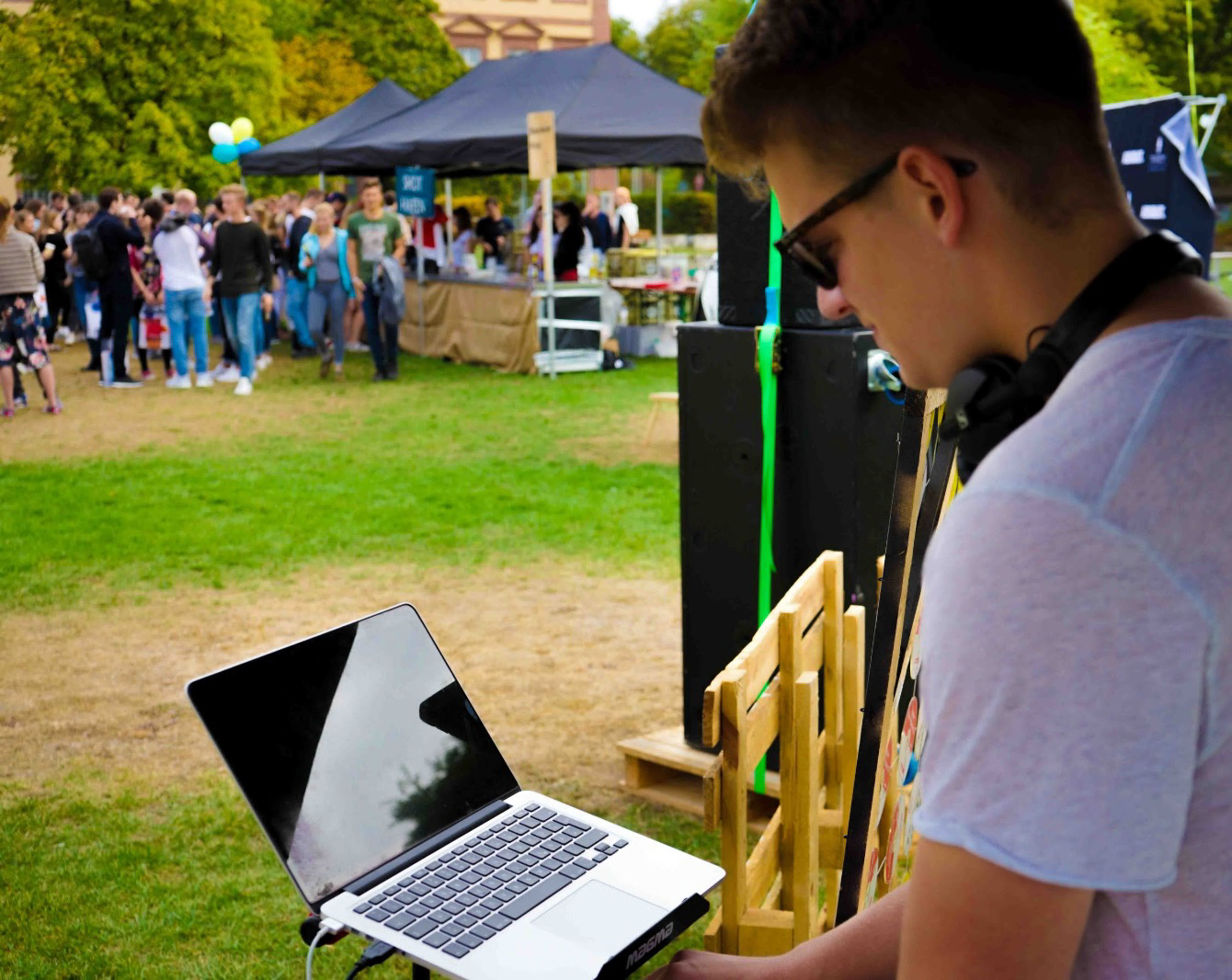 noelgon performing an outdoor set with headphones, crowd and tents in the background.